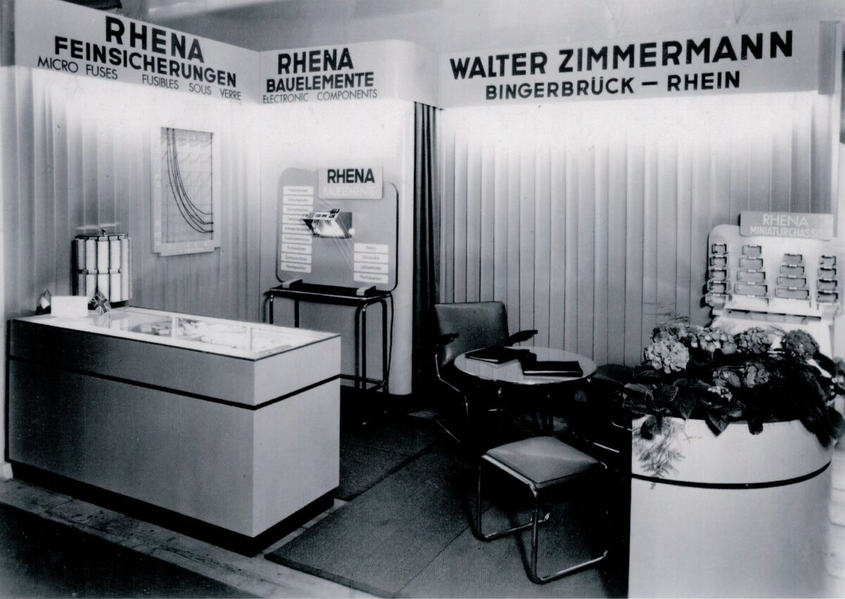 Das Bild zeigt den Stand des Unternehmens Rhena auf der Industriemesse Hannover im Jahr 1953. Die Schwarz-Weiß-Aufnahme vermittelt einen historischen Eindruck der Messepräsentation und spiegelt das industrielle Design sowie die Geschäftsatmosphäre dieser Zeit wieder.
