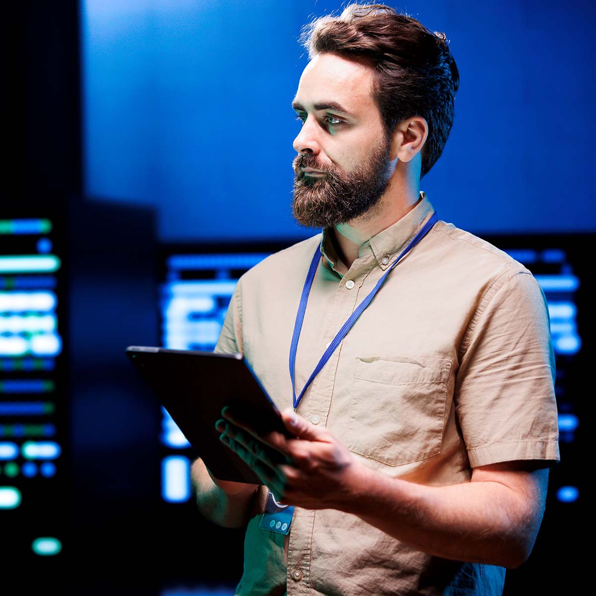 Lifestyle Foto IT-Operations Das Bild zeigt einen Mitarbeiter in der IT-Operations-Abteilung, der den Serverraum kontrolliert. Er hält ein Tablet in der Hand, um die Serverstatus und -leistungen zu überwachen oder zu analysieren. Die Szene vermittelt eine professionelle und technische Arbeitsumgebung, in der der Mitarbeiter für die Aufrechterhaltung der Netzwerksicherheit und -stabilität verantwortlich ist.
