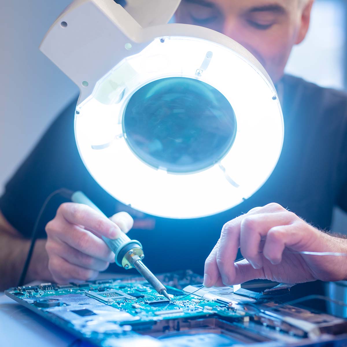 Situationsbild PCB Reparatur Das Bild zeigt einen Mitarbeiter, der Ersatzteile einlötet. Mit präziser Handarbeit arbeitet er an einer technischen Komponente, um diese zu reparieren oder zu optimieren. Die Szene vermittelt eine detailorientierte und technische Arbeitsumgebung, in der Fachwissen und Sorgfalt erforderlich sind.