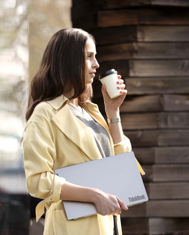 Eine Frau in einem gelben Blazer trinkt entspannt Kaffee und hält in ihrer rechten Hand ein Lenovo ThinkBook. Die Szene strahlt Professionalität und Eleganz aus, während sie das ThinkBook als Teil ihres täglichen Arbeitsalltags nutzt.
